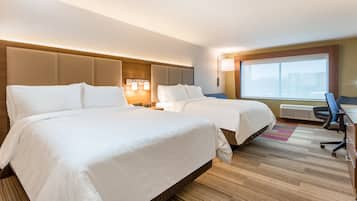 A hotel room with two beds, a desk, and a large window.