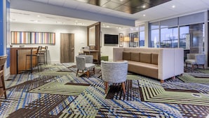 A modern hotel lobby with a patterned carpet, a sofa, chairs, a bar area, and large windows. - Holiday Inn Express & Suites Florence-Cincinnati Airport by IHG (Florence)