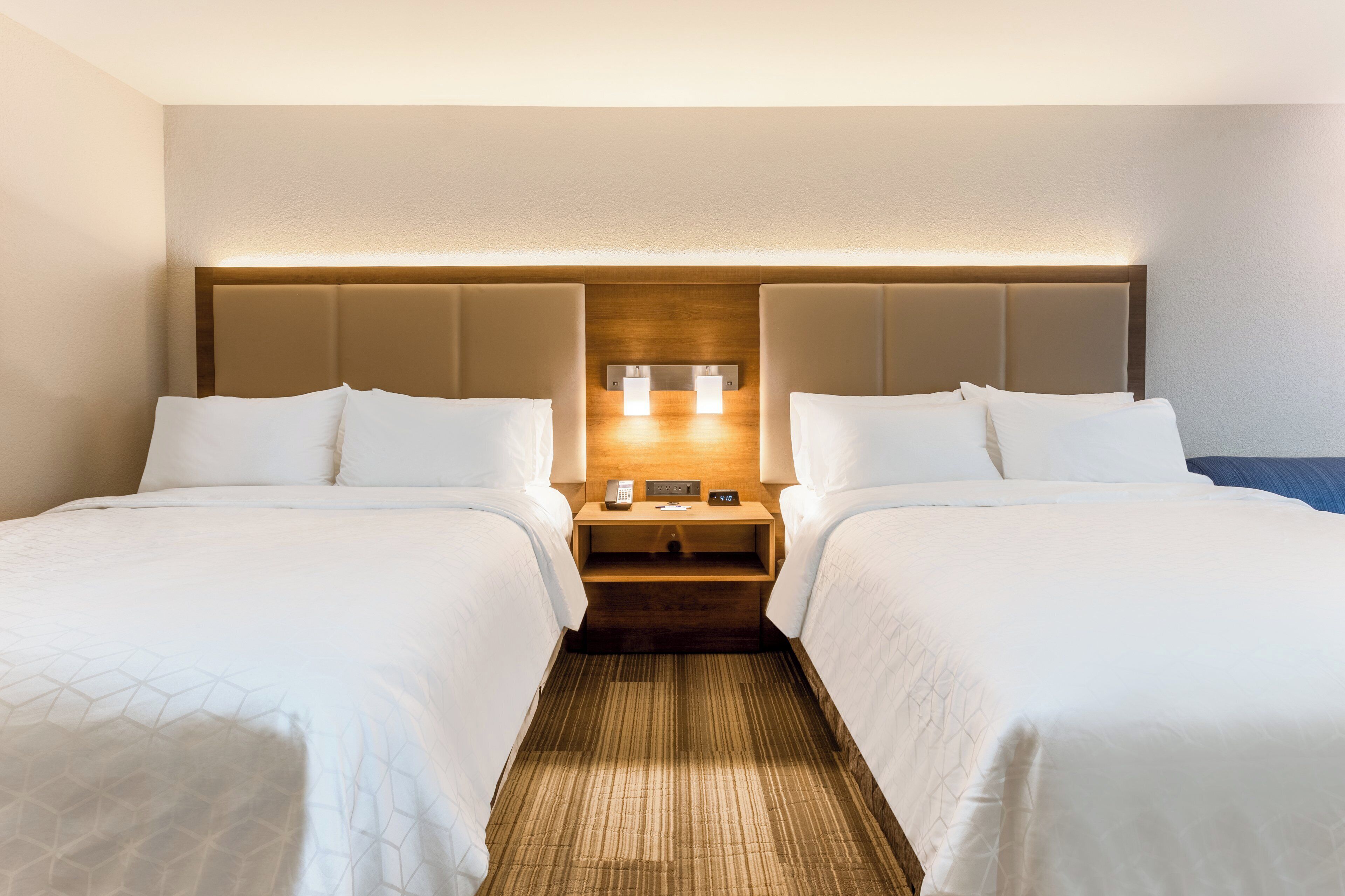 A hotel room with two beds, a wooden headboard, bedside tables with lamps, and a clock.