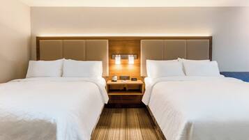A hotel room with two beds, a wooden headboard, bedside tables with lamps, and a clock.