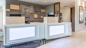 A reception area with two light-colored reception desks, a modern wall design, and a carpeted floor. - Holiday Inn Express & Suites Florence-Cincinnati Airport by IHG (Florence)