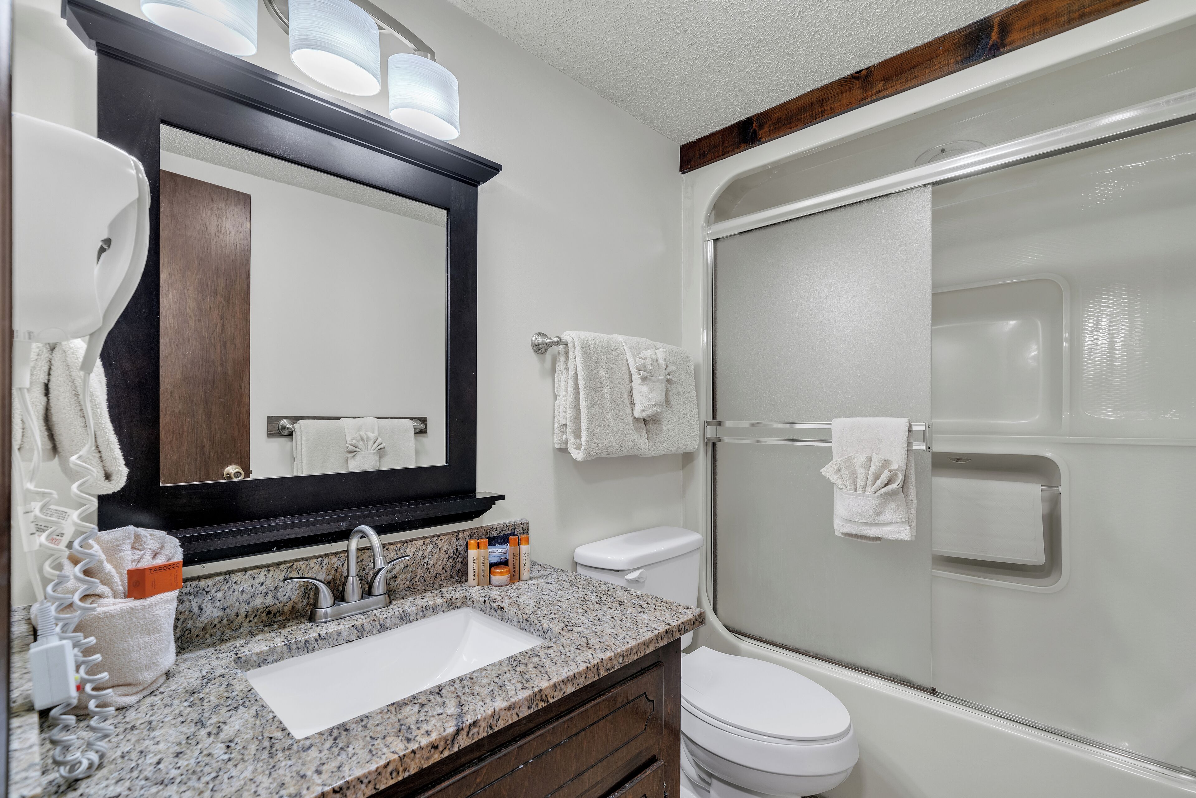 Une salle de bain avec un lavabo en granit, un grand miroir, des toilettes et une douche à parois de verre.
