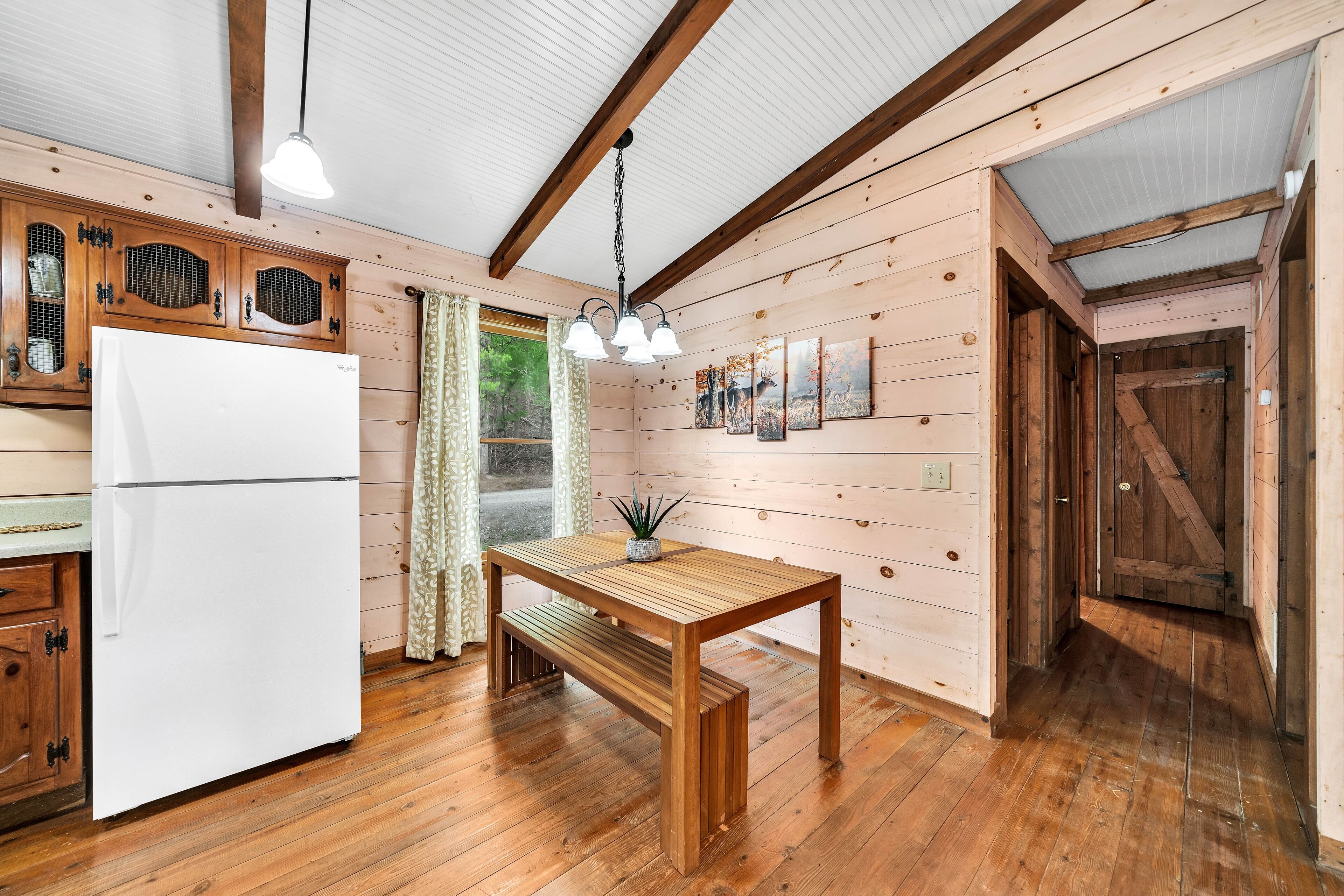 A wooden cabin interior with a wooden table, bench, and white refrigerator.