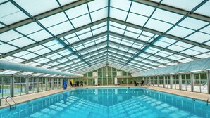 An indoor swimming pool with a glass ceiling, surrounded by lounge chairs and a view of the outdoors.