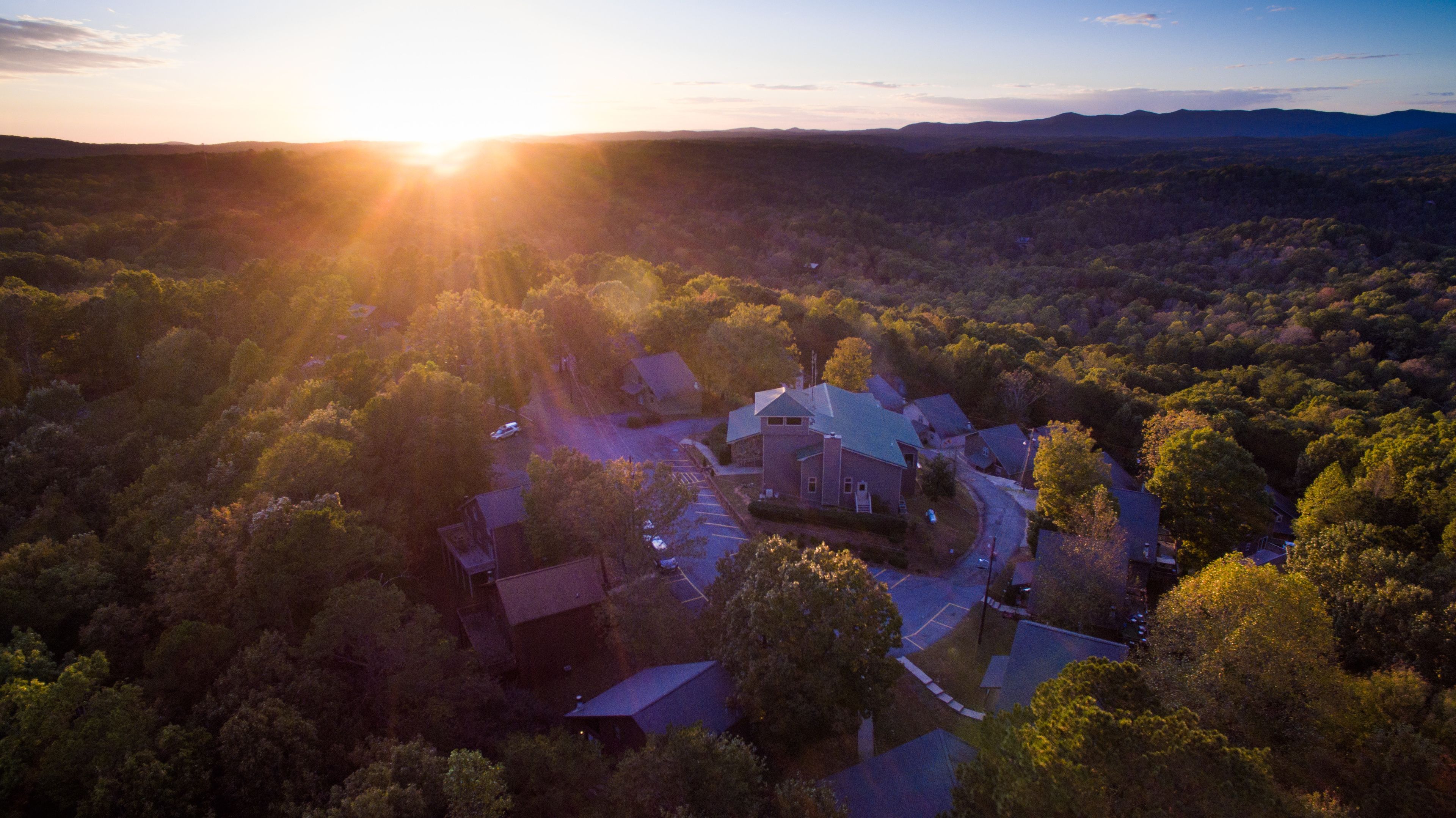 An aerial view of a residential area with houses surrounded by dense forest, during sunset.