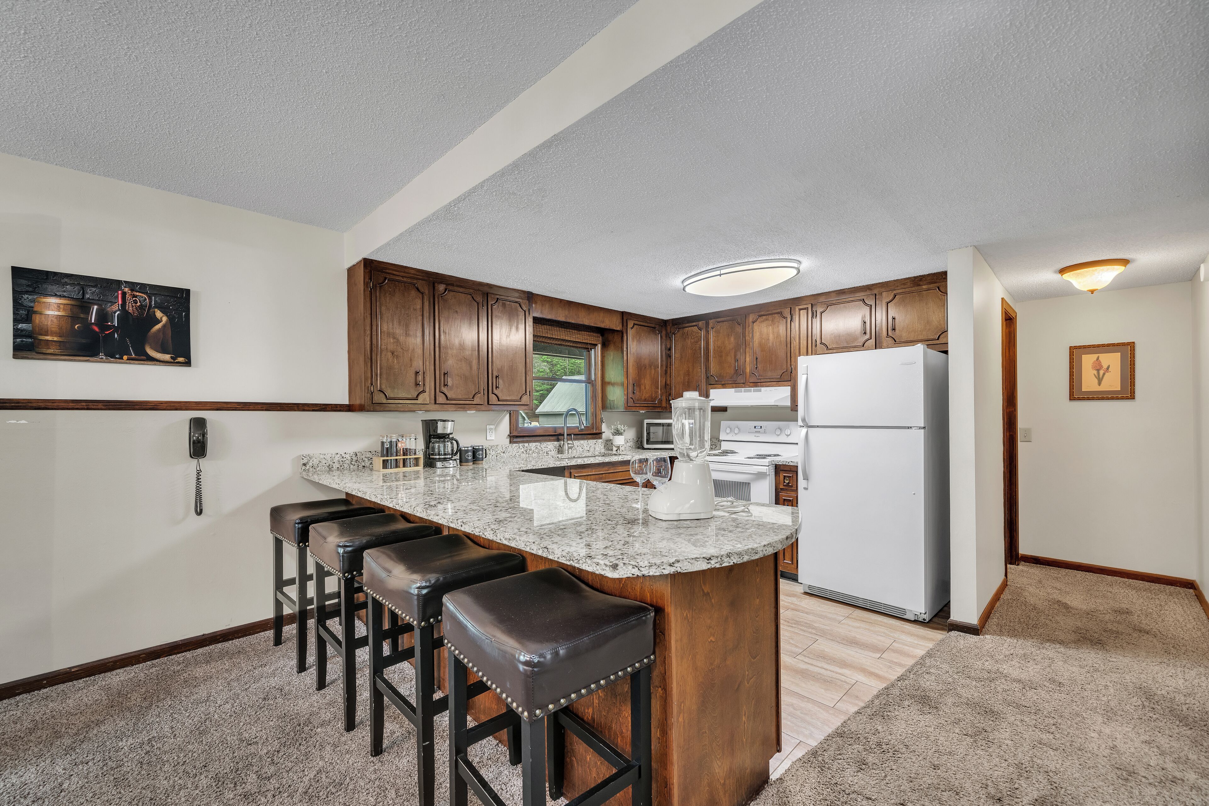 A kitchen with a central island, bar stools, wooden cabinets, a refrigerator, and a microwave.