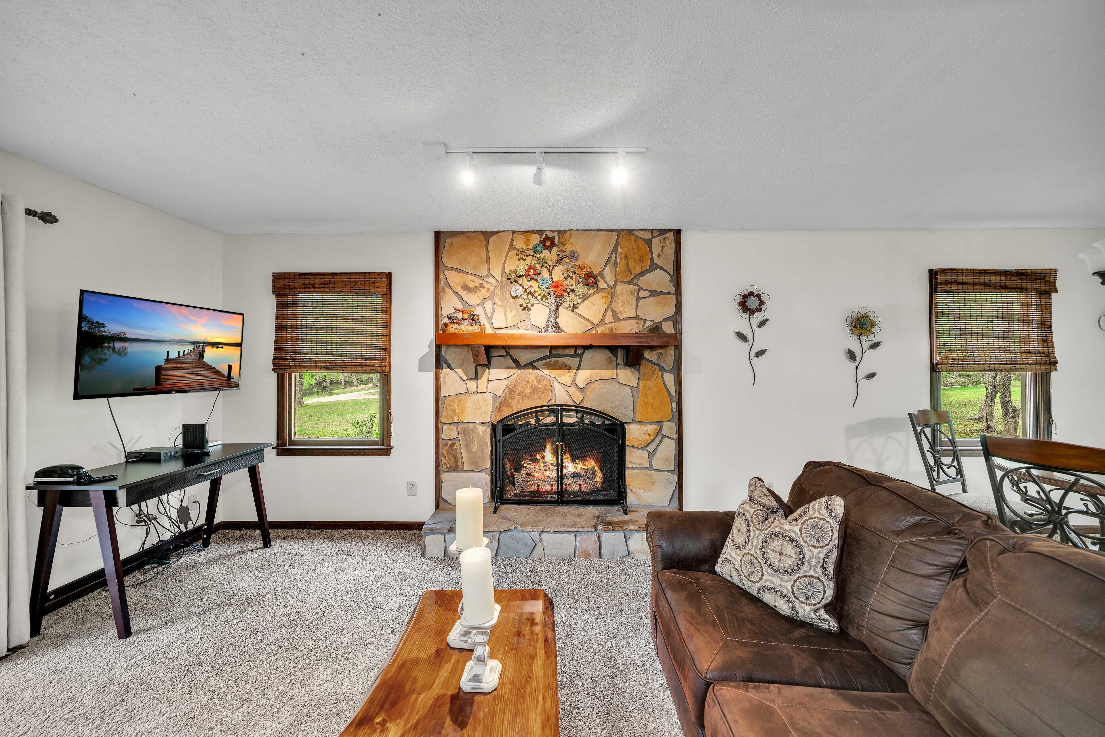 A living room with a stone fireplace, a television, a brown leather couch, and a coffee table with candles.