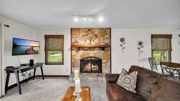 A living room with a stone fireplace, a television, a brown leather couch, and a coffee table with candles.