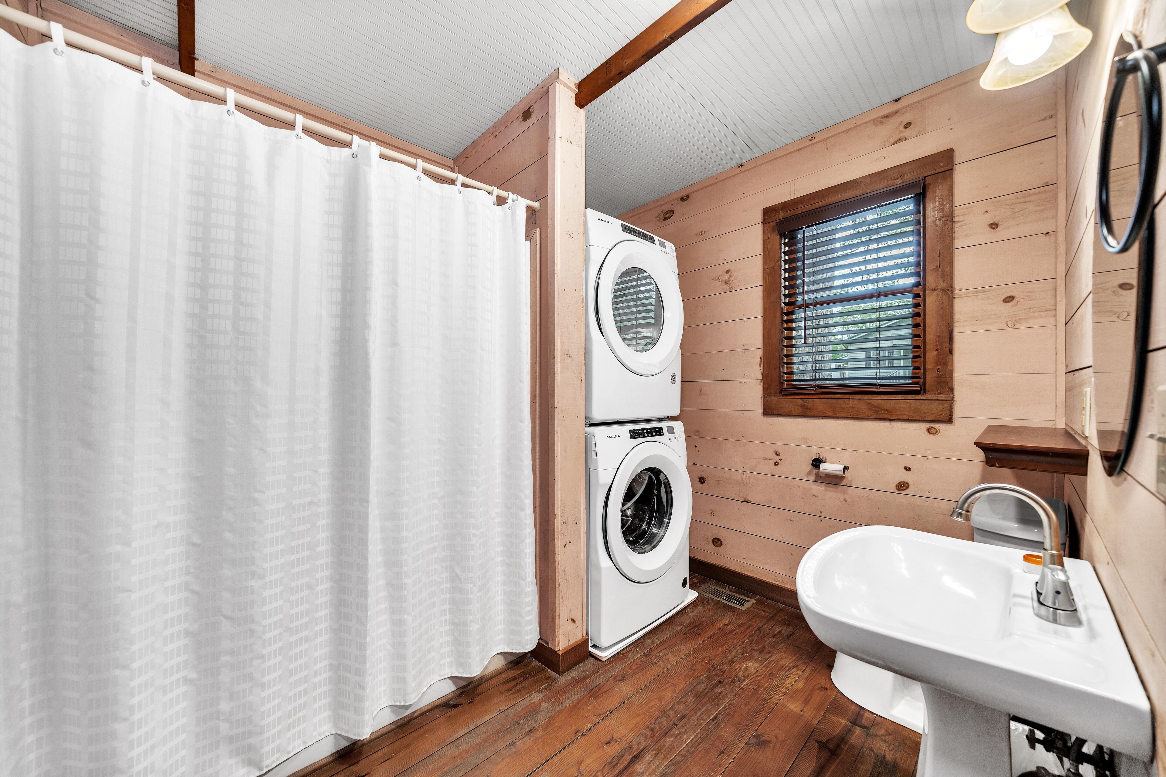 A compact bathroom with wooden walls, a white sink, and a front-loading washing machine.