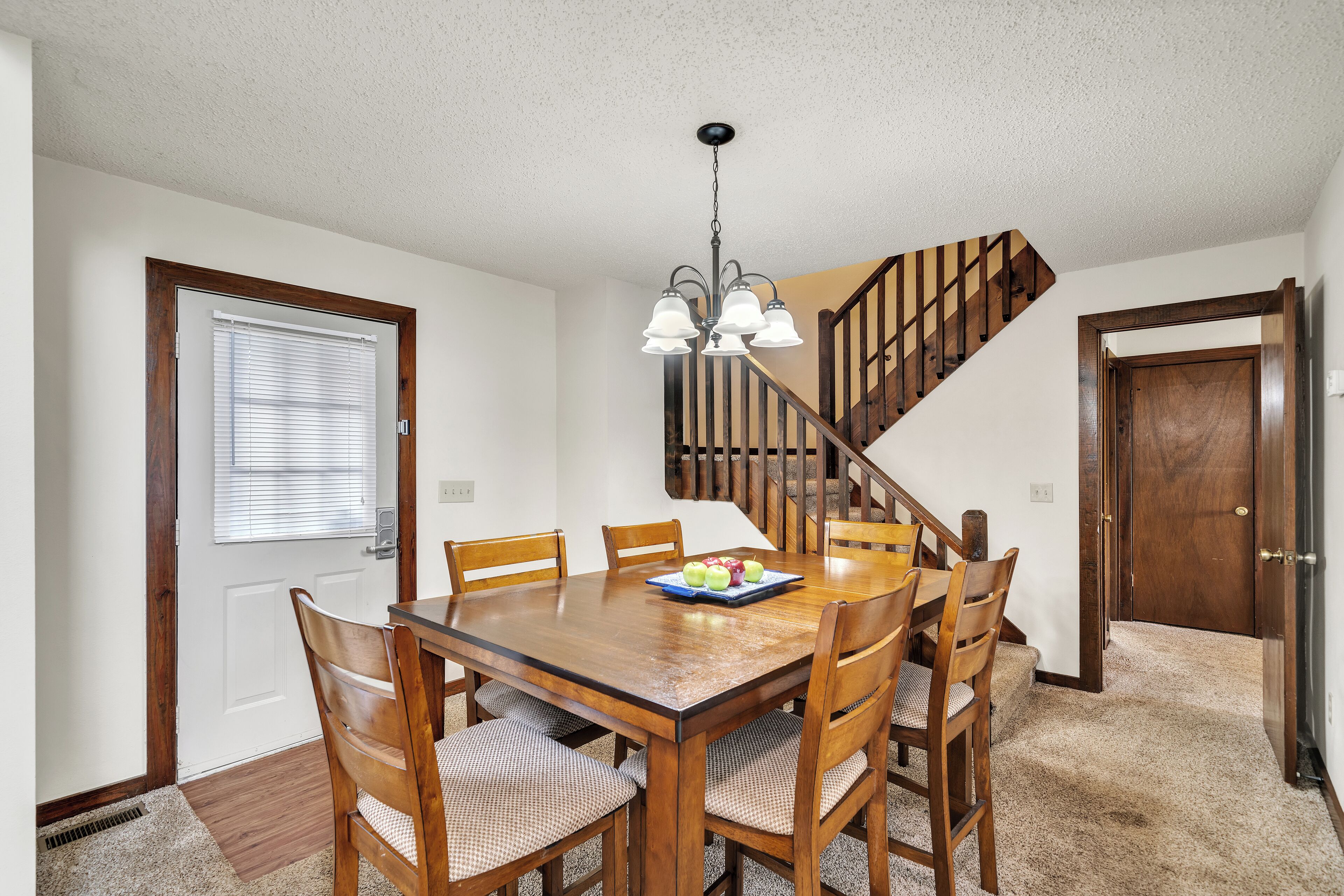 A dining area with a wooden table and chairs, a chandelier, and a staircase.