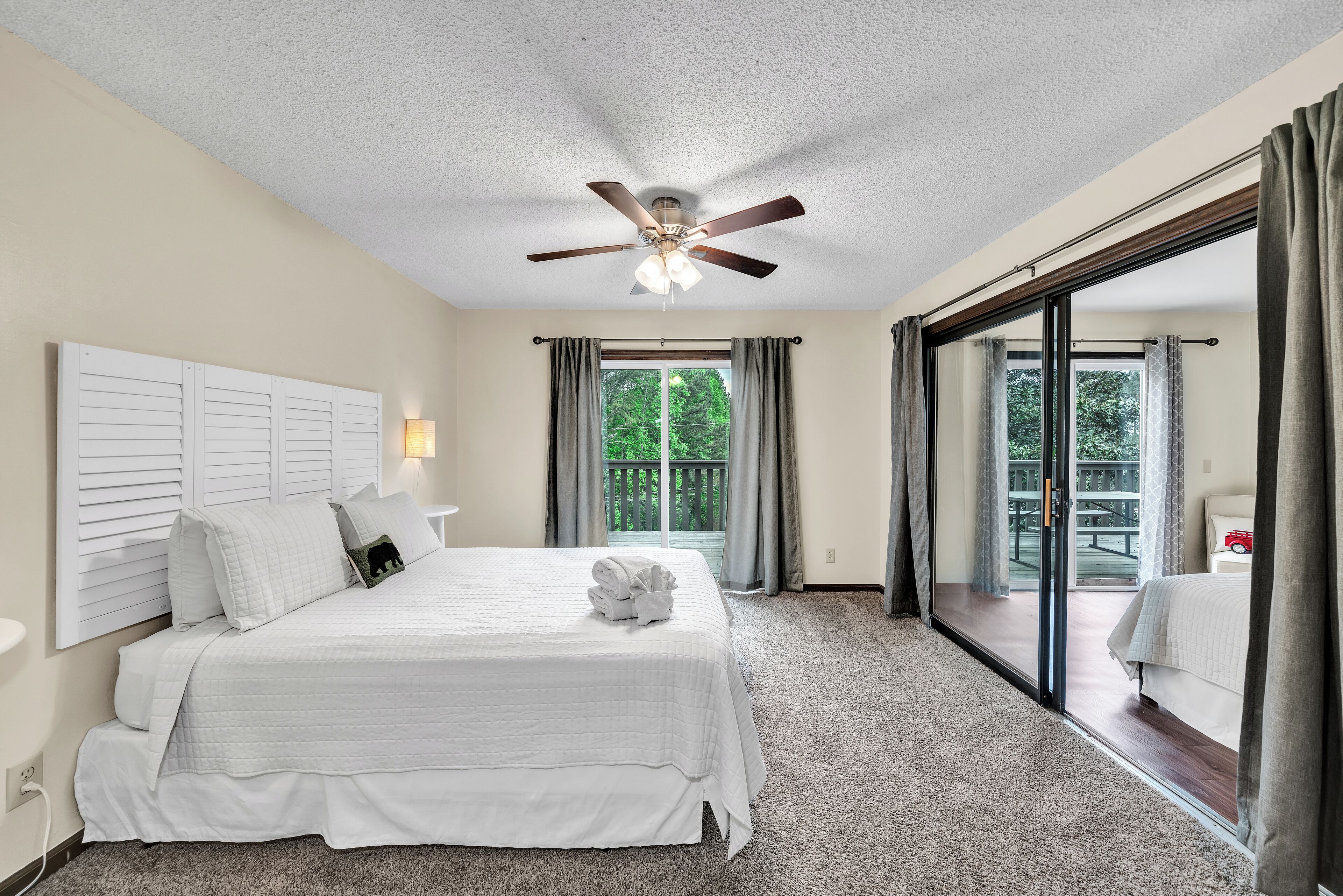 A bedroom with a large bed, a ceiling fan, and a sliding glass door to a balcony.