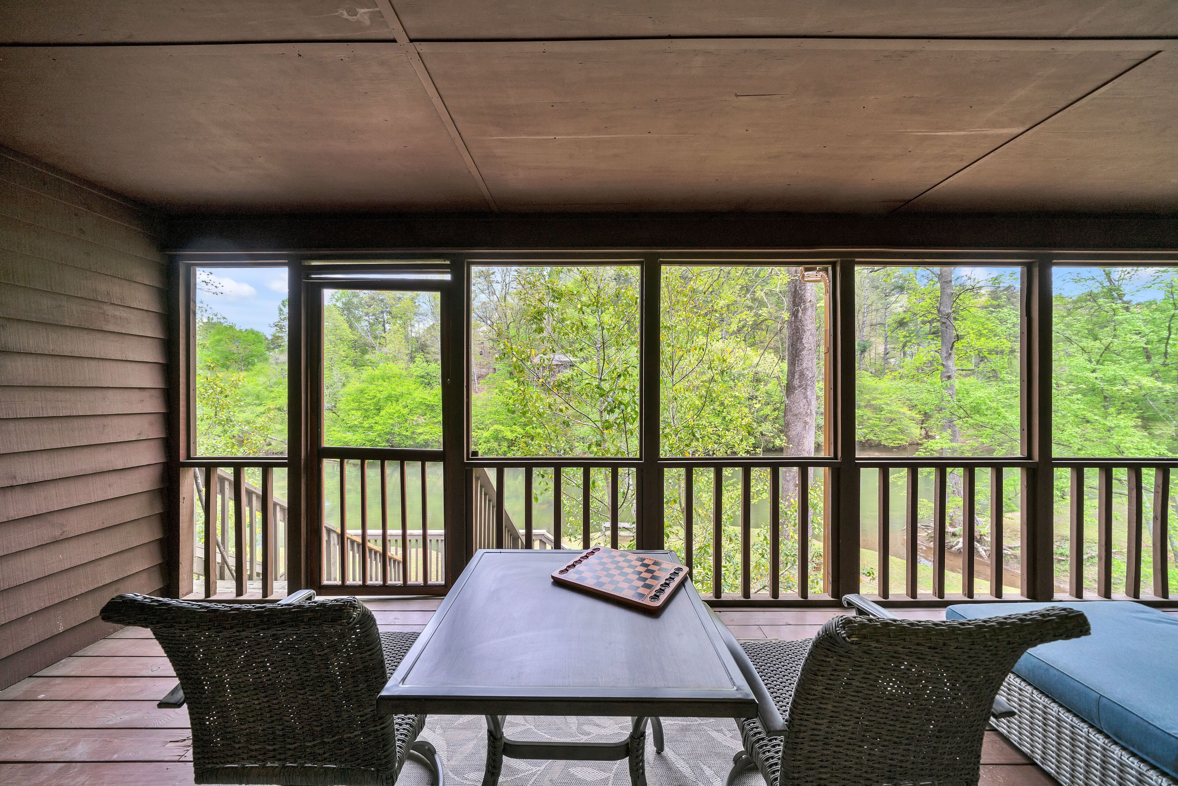 A covered outdoor area with a table and chairs, a chessboard, and a view of a wooded area.