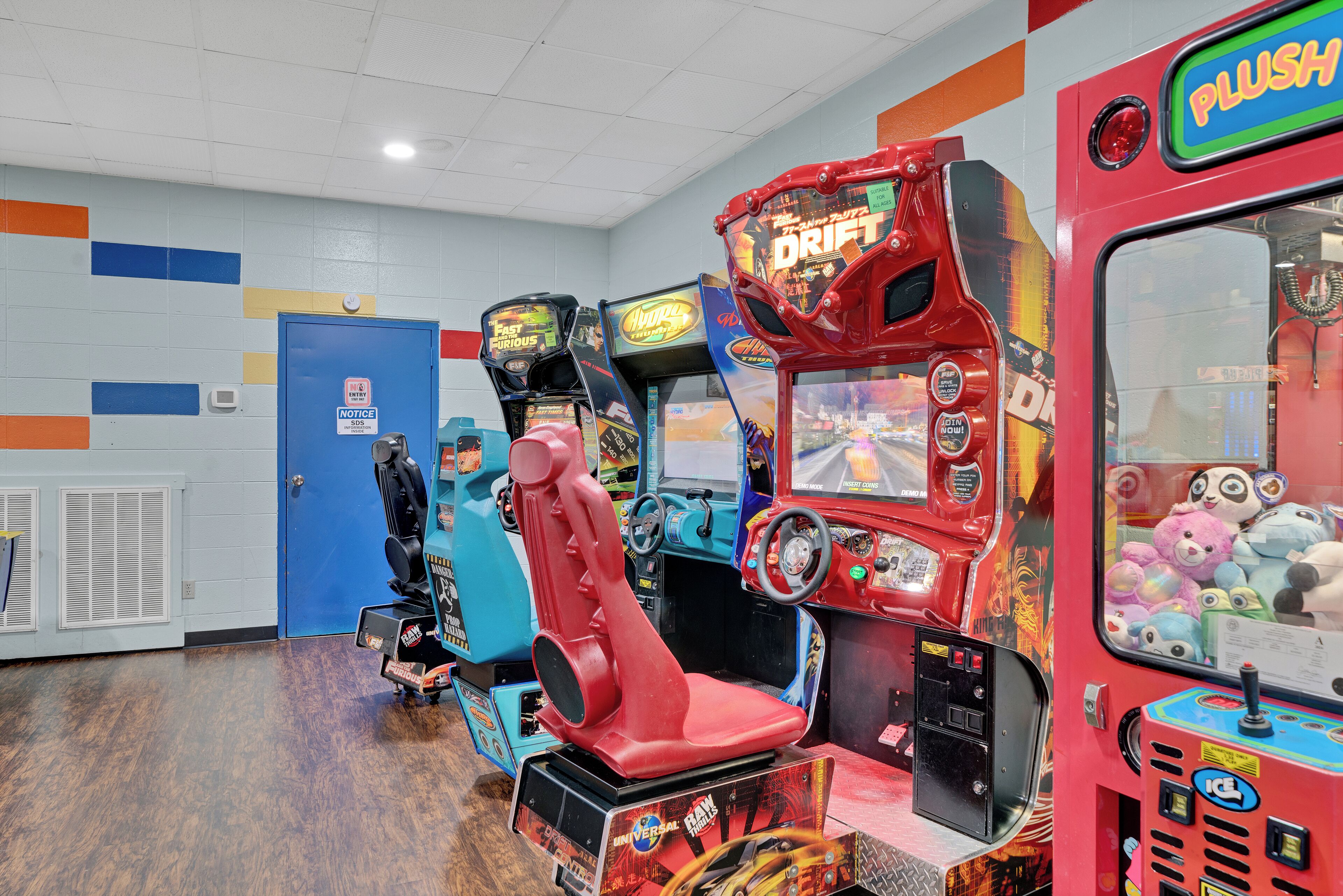 En rad med arkadspel, med en blå dörr och en röd spelmaskin i bakgrunden, där det står ”DRIFT” på.