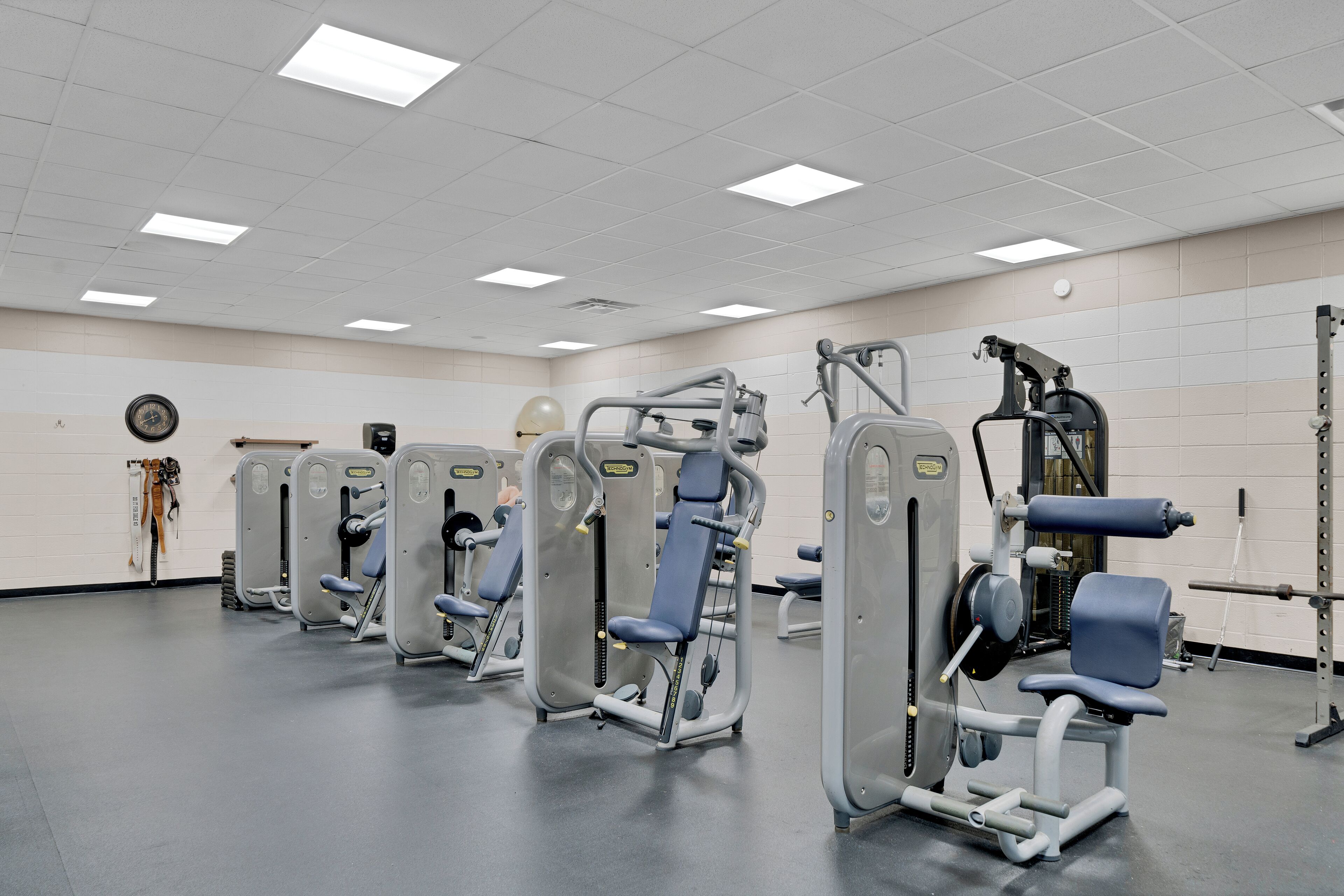 A gym with multiple exercise machines, a clock on the wall, and a weight rack.