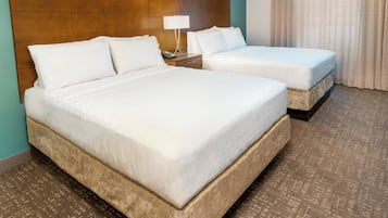 Habitación de hotel con dos camas, una mesita de noche con lámpara y una alfombra estampada.