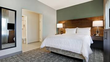 A hotel room with a large bed, two bedside lamps, a wooden headboard, a mirror, and a view of the bathroom.