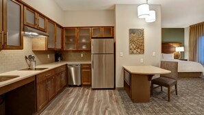 Habitación de hotel compacta con kitchenette, cama, una mesita con silla y un cuadro en la pared.