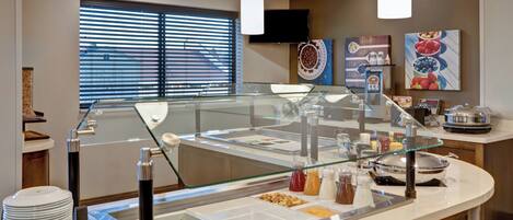 A buffet area with various food options, a glass barrier, and a television mounted on the wall.