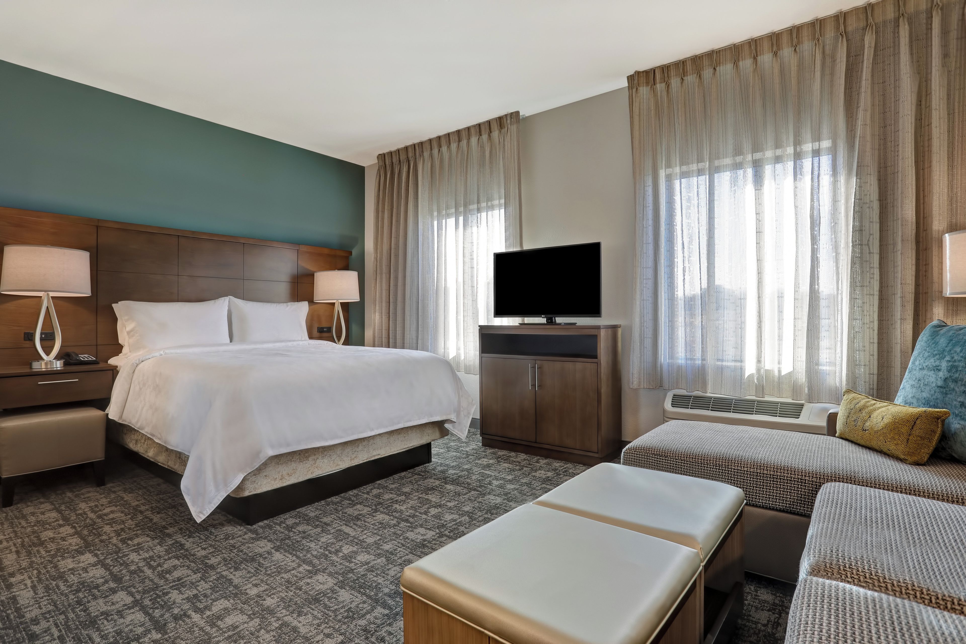 Una habitación de hotel con una cama, mesitas de noche, televisor, sofá y una pequeña mesa.