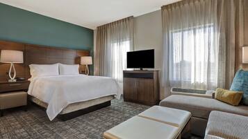 Una habitación de hotel con una cama, mesitas de noche, televisor, sofá y una pequeña mesa.