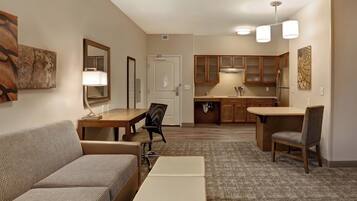 A hotel room with a sofa, a small table, a chair, a kitchenette, and a dining area.