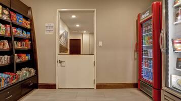 A corridor with a vending machine, snack shelves, and a door leading to another room.