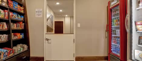 A corridor with a vending machine, snack shelves, and a door leading to another room.