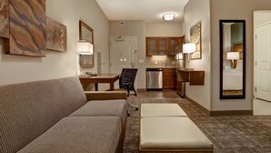 Un espacio habitable pequeño con sofá, una mesita, una silla, kitchenette y un espejo.