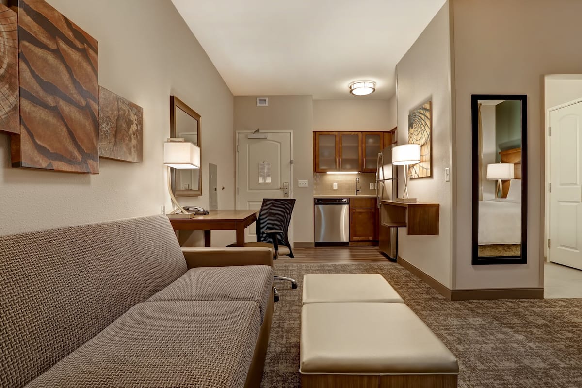 A compact living space with a sofa, a small table, a chair, a kitchenette, and a mirror.