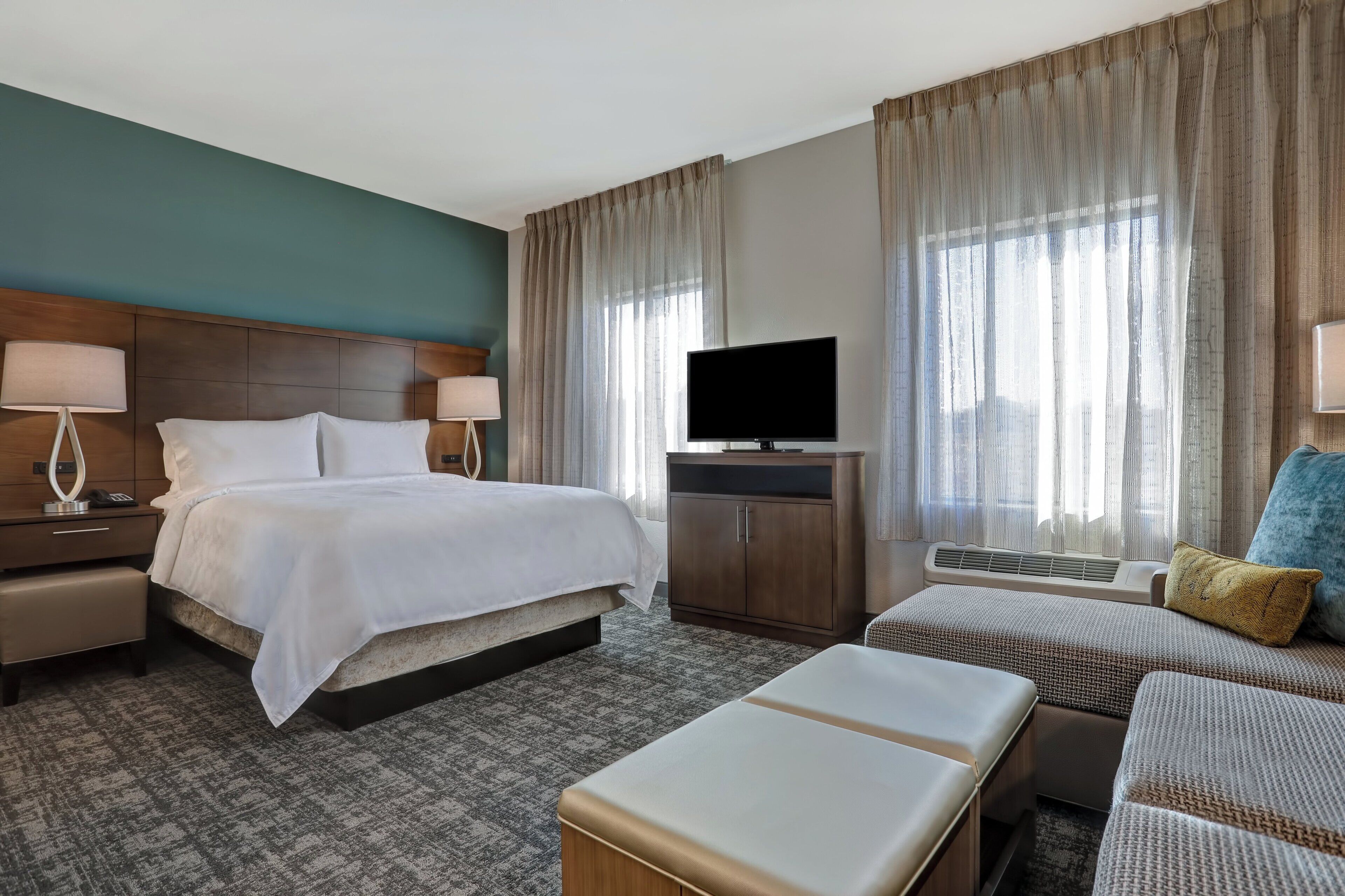 Ein Hotelzimmer mit einem Bett, Nachttischen, einem Fernseher, einem Sofa und einem kleinen Tisch mit einer Lampe.