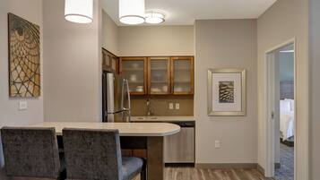 A modern kitchen with a dining area, featuring a refrigerator, stove, and a dishwasher. There are two chairs and a table in the dining area.