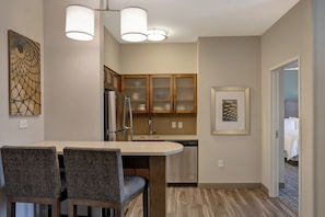 A modern kitchen with a dining area, featuring a refrigerator, stove, and a dishwasher. There are two chairs and a table in the dining area.