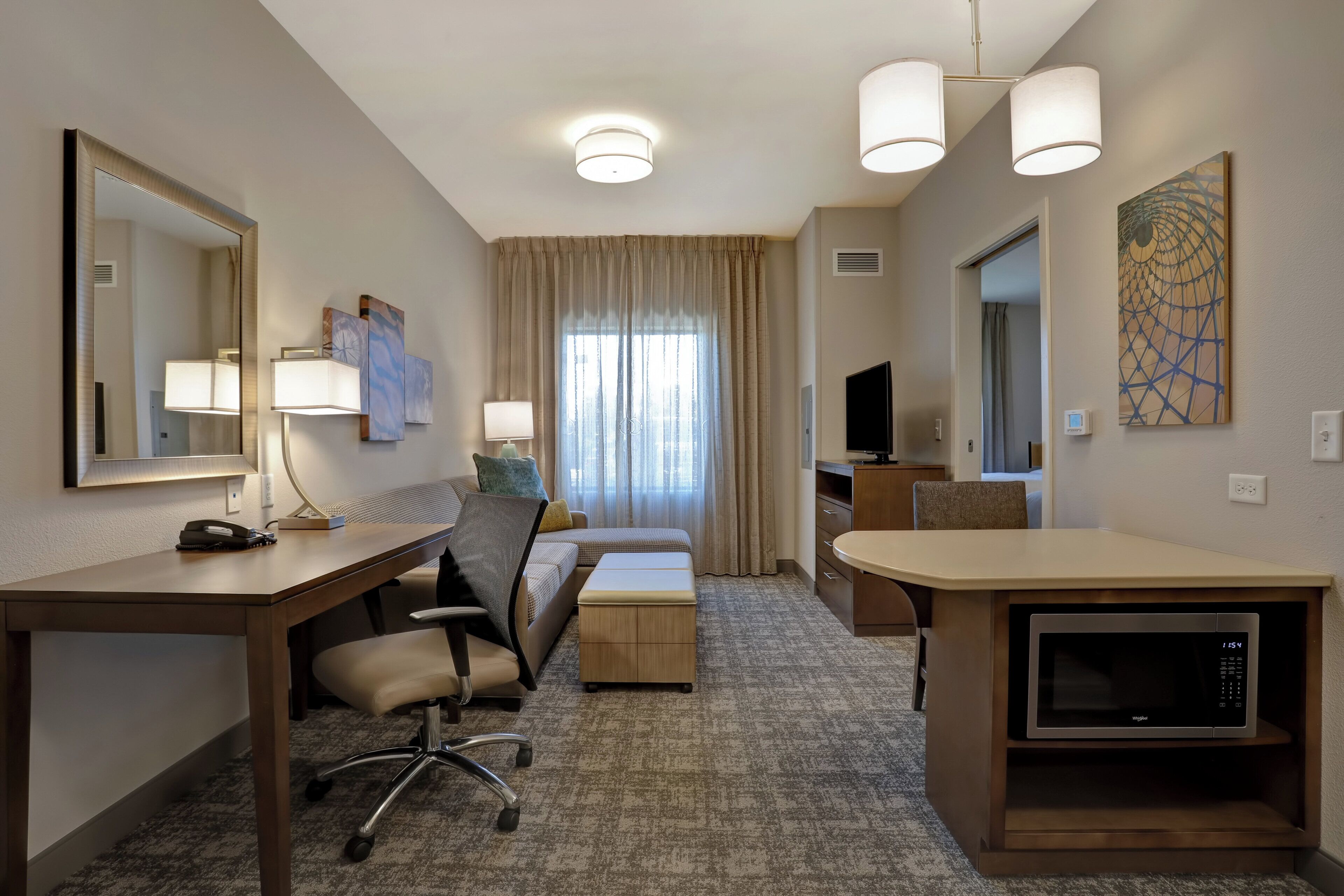 A hotel room with a desk, chair, bed, TV, and a microwave.