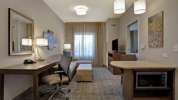 A hotel room with a desk, chair, bed, TV, and a microwave.