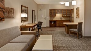 Habitación de hotel compacta con sofá, una pequeña mesa de comedor, kitchenette y espejo.