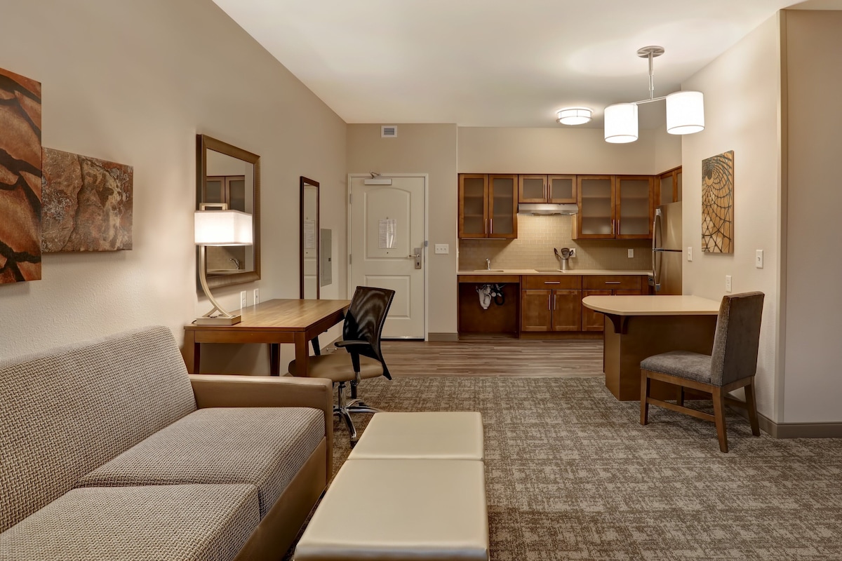 Habitación de hotel compacta con sofá, una pequeña mesa de comedor, kitchenette y espejo.
