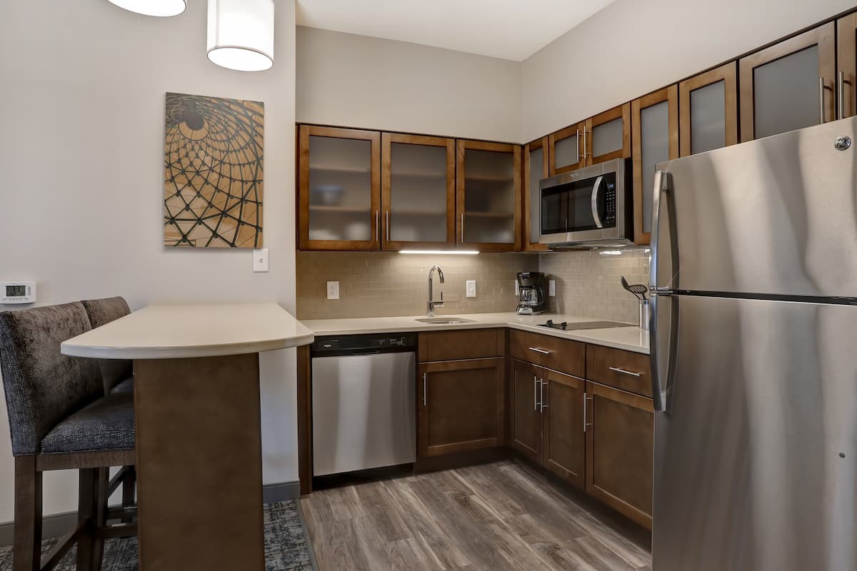 A modern kitchen with wooden cabinets, a stainless steel refrigerator, a dishwasher, and a microwave.