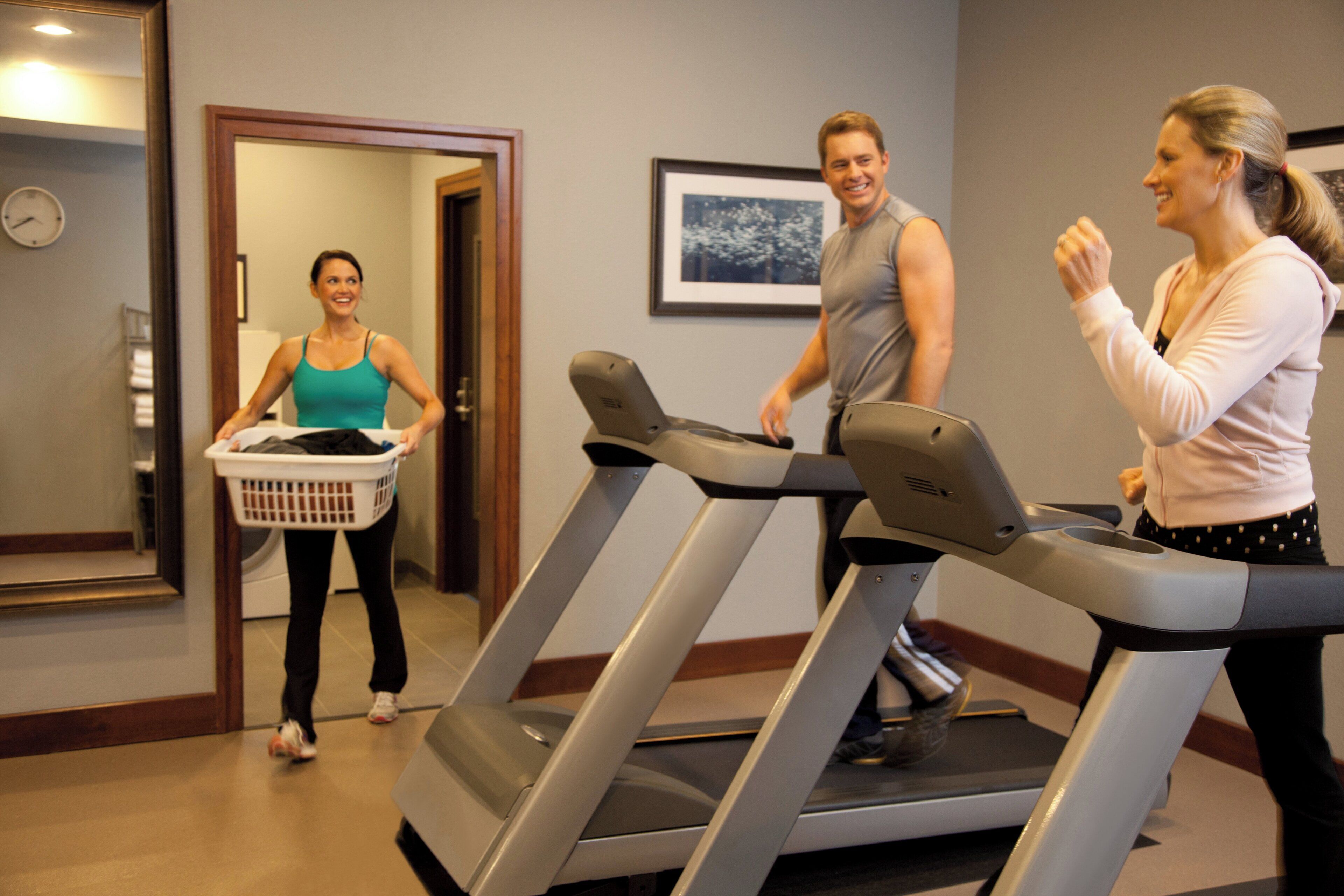 A fitness room with treadmills, a wall clock, and a door leading to another room.