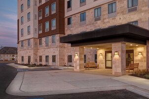 Un hotel de varios pisos con vestíbulo cubierto, zona de estar al aire libre y aparcamiento.