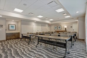 Une salle de conférence équipée de tables et de chaises, dotée d’un sol recouvert de moquette et d’un éclairage au plafond.