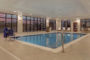 Una piscina interior con paredes de vidrio transparente, un área de descanso junto a la piscina y vistas de la ciudad.