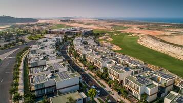 A modern residential area with solar panels on the rooftops, a golf course nearby, and a clear view of the coastline.
