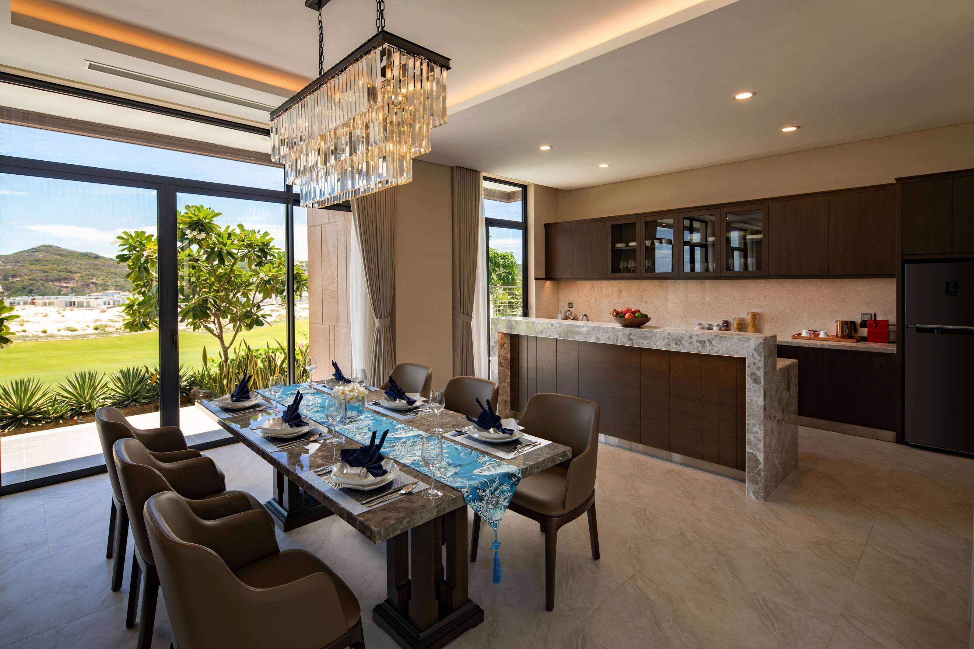 A modern kitchen with a marble countertop, dark cabinets, and a dining area with a long table and chairs.