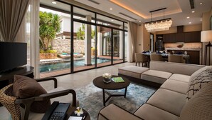A modern living room with a large TV, comfortable seating, a pool view, and a kitchen area. - Wyndham Grand KN Paradise Cam Ranh (Bac Cam Ranh)