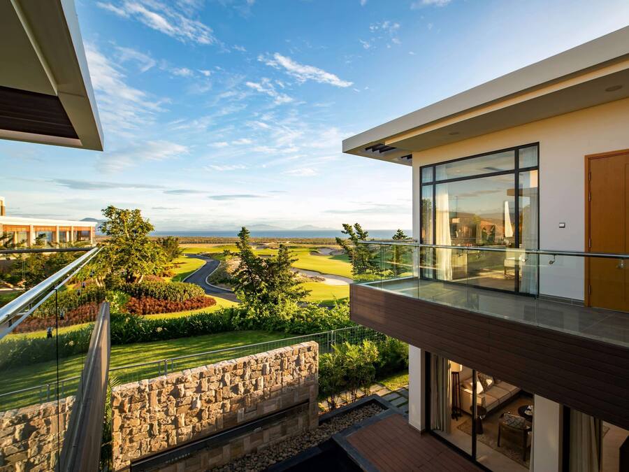 A modern building with a glass balcony overlooking a landscaped area with a golf course.