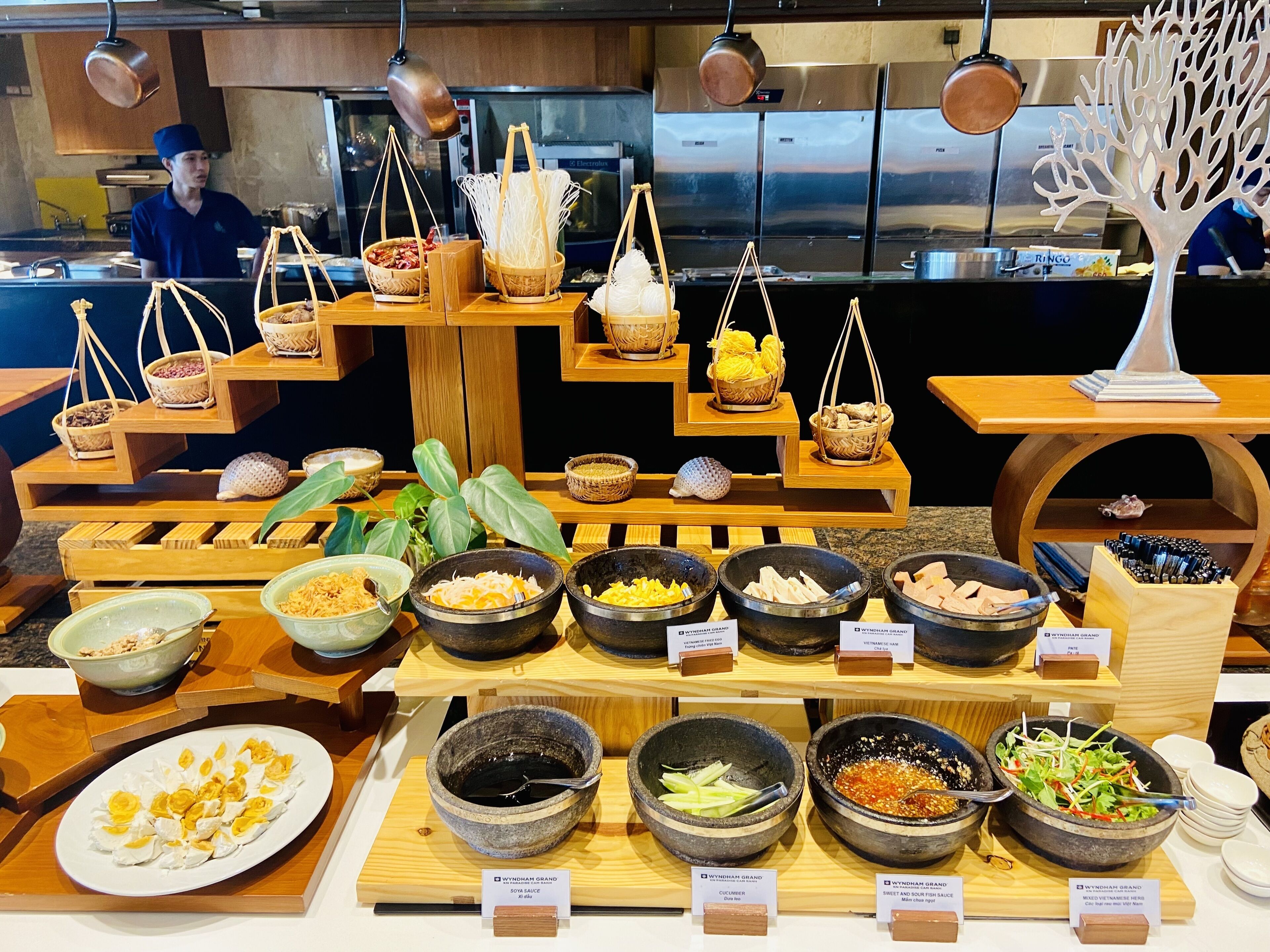 A food display with various dishes and sauces, including a plate of yellow flowers, bowls of different sauces, and baskets of ingredients.