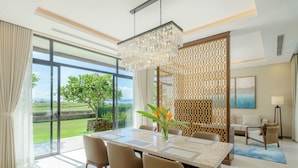 A modern dining area with a large table, chairs, and a chandelier. There is a view of greenery outside through large windows. - Wyndham Grand KN Paradise Cam Ranh (Bac Cam Ranh)