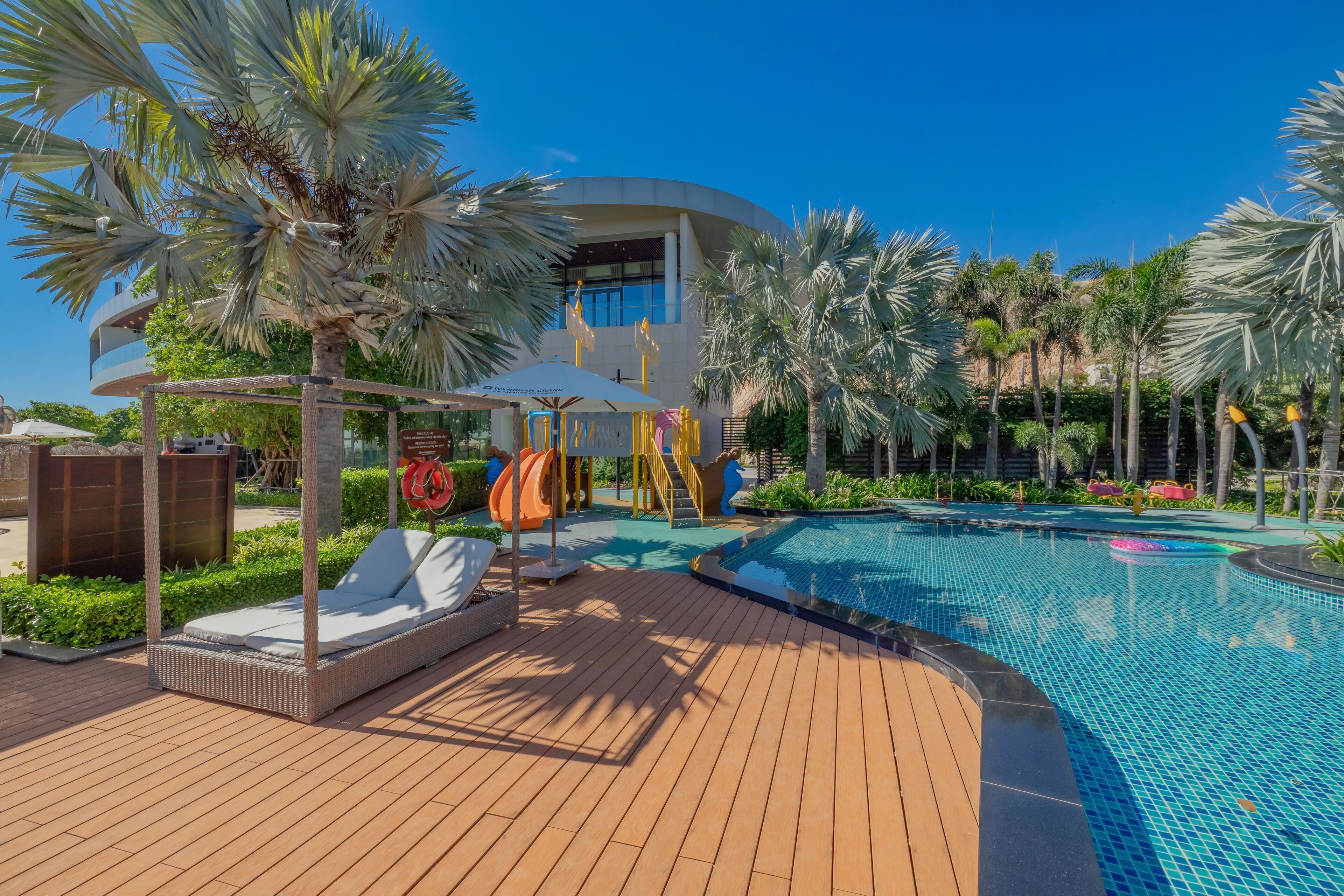 A pool area with lounge chairs, palm trees, and a modern building in the background.