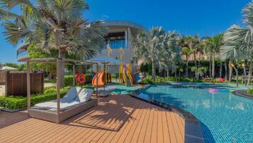 A pool area with lounge chairs, palm trees, and a modern building in the background.