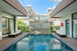 Un área de piscina moderna con un muro de piedra, sillas de descanso y un flotador en la pared.